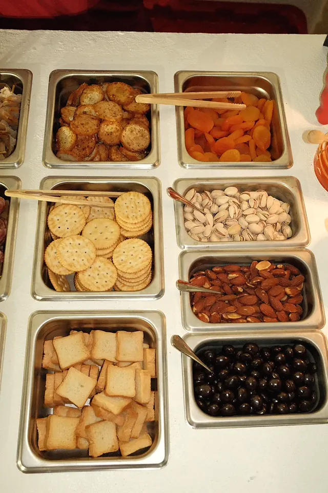 Steel pans of crackers, apricots, pistachios, olives and cheese on the charcuterie cart